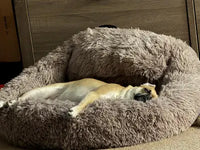 Customer review photo of a tan puggle dog lying stretched out in a taupe faux fur donut bed
