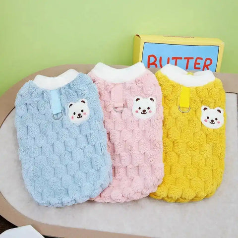 Three colorful dog sweaters with bear face designs on green background.