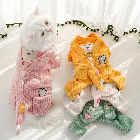 Three colorful pet outfits on white surface with cat wearing pink outfit.