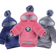 Three pet hoodies in blue, pink, and gray with pom-poms on white.