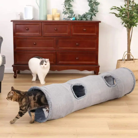 Two cats interacting with a gray pet tunnel on wooden floor.