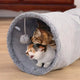 Two cats playing with a plush tunnel toy on wooden floor.