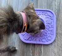 Customer review photo of a scruffy wirehaired terrier mix dog with a pink collar licking a purple Woof LickMat.