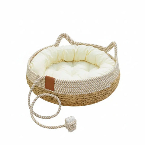 Woven pet bed with plush cushion on wooden floor with rope toy.