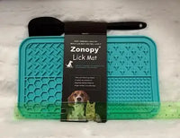 Product photo of a teal Zonopy Lick Mat with its black brand sleeve, an included black spatula tool, and a green plastic ruler showing dimensions.